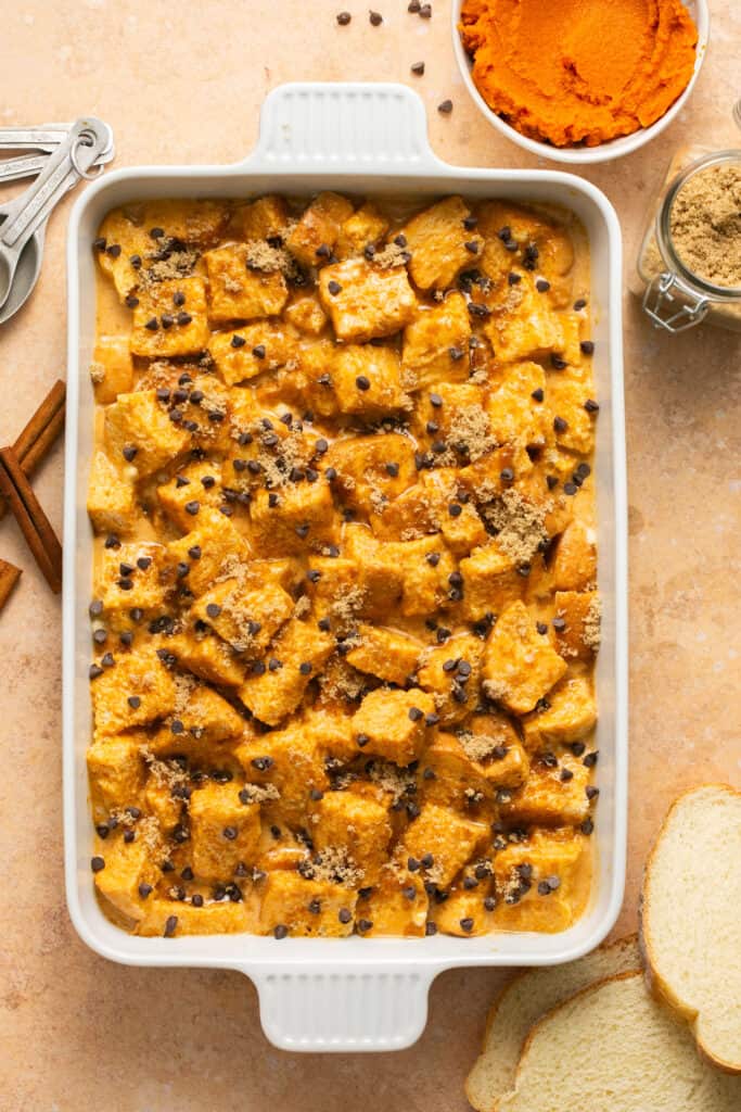 Chocolate chips sprinkled on top of the pumpkin chocolate chip protein french toast bake in a baking dish before being baked.