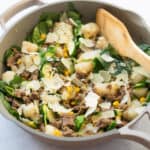 Sausage and zucchini cauliflower gnocchi skillet topped with shaved parmesan cheese ina skillet with a wooden spoon.