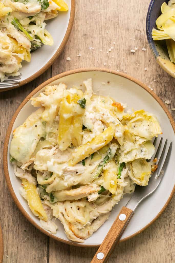 Healthy spinach and artichoke pasta bake on a plate with a fork.