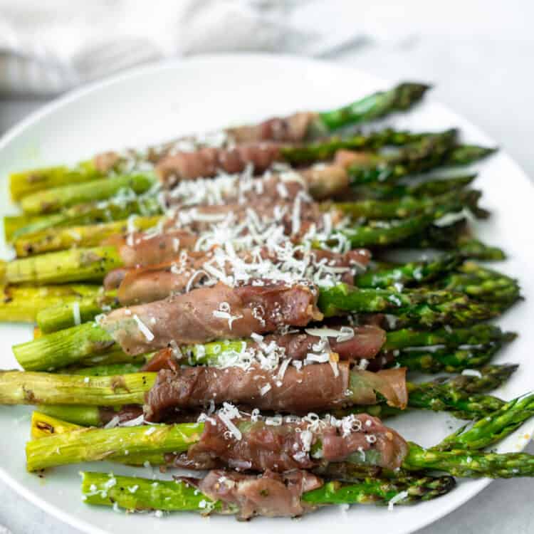 Prosciutto wrapped asparagus topped with grated cheese on a plate.