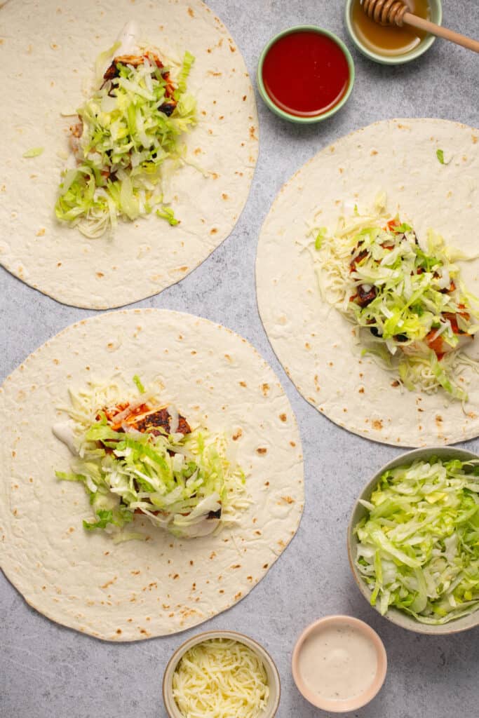 tortillas topped with buffalo chicken, lettuce, and ranch before being wrapped up.