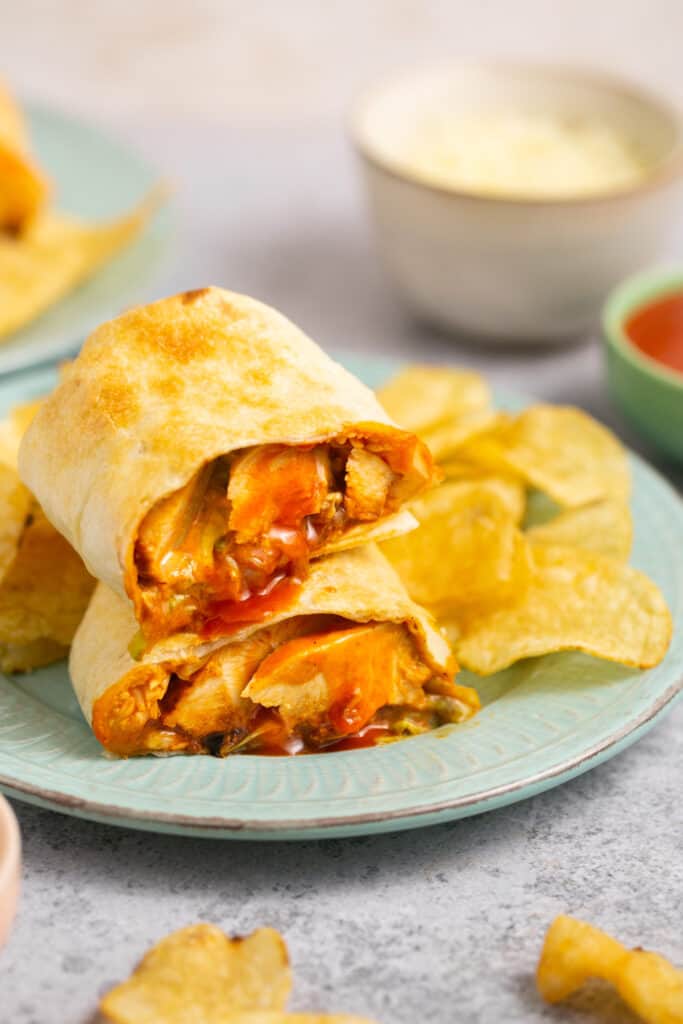 Air fryer buffalo chicken wrap cut in half and stacked on top of each other on a plate with chips.