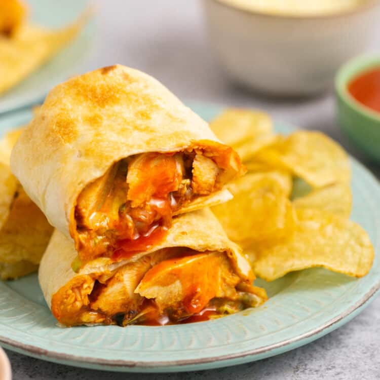 Air fryer buffalo chicken wrap cut in half and stacked on top of each other on a plate with chips.