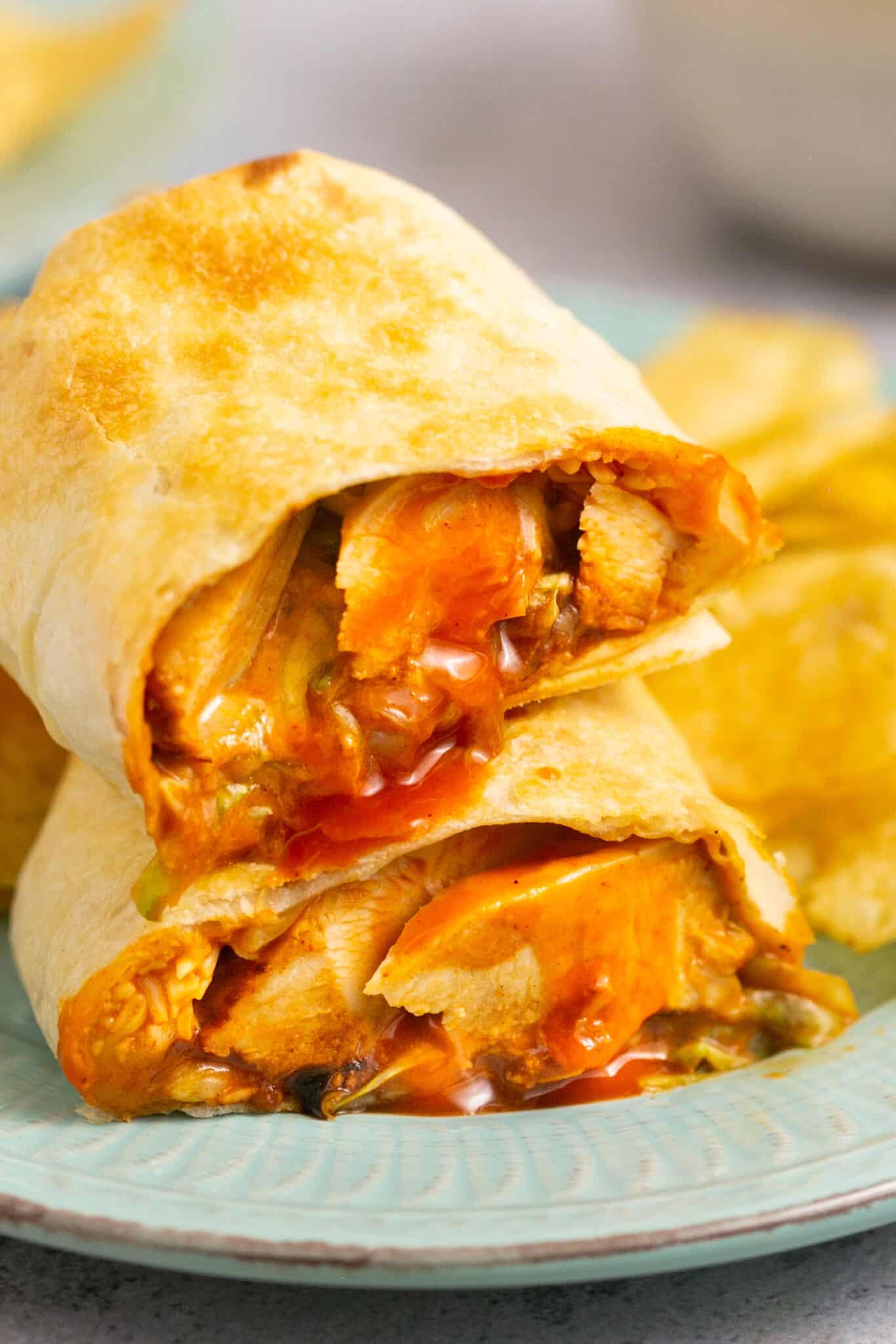 Air fryer buffalo chicken wrap cut in half and stacked on top of each other on a plate with chips.