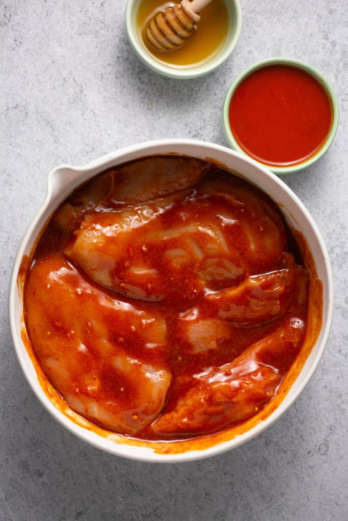 Chicken breasts tossed in the buffalo sauce in a mixing bowl.