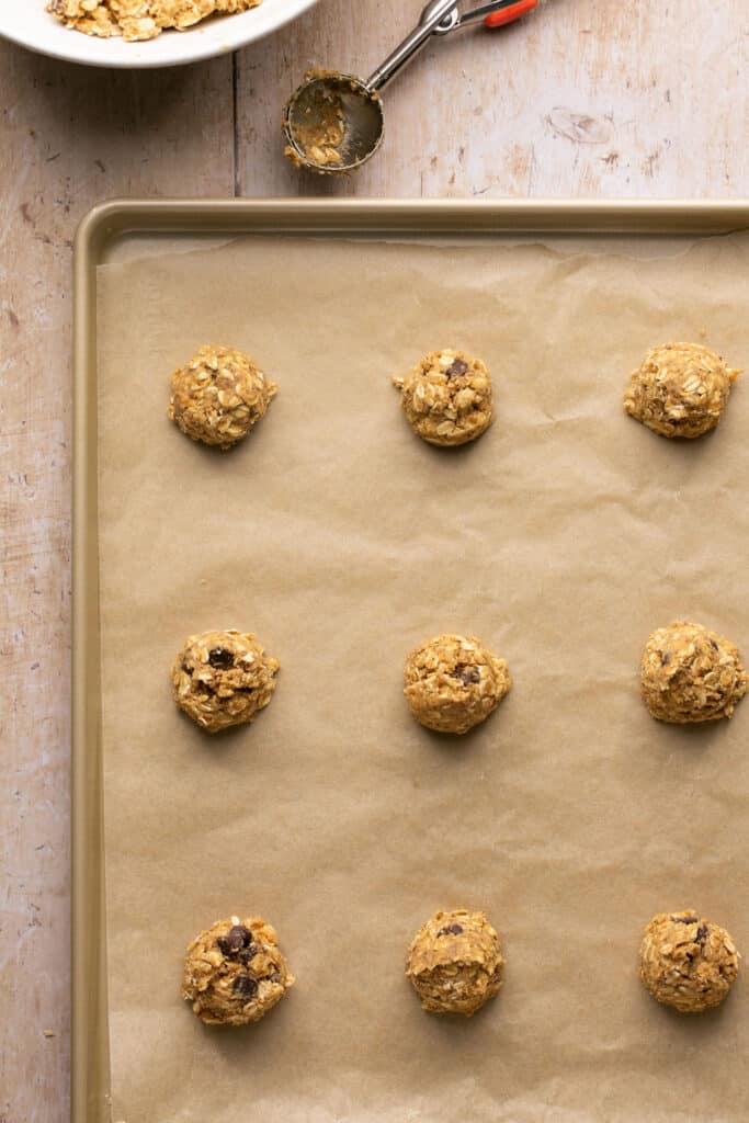 Cookie dough balls on a baking sheet with parchment paper.