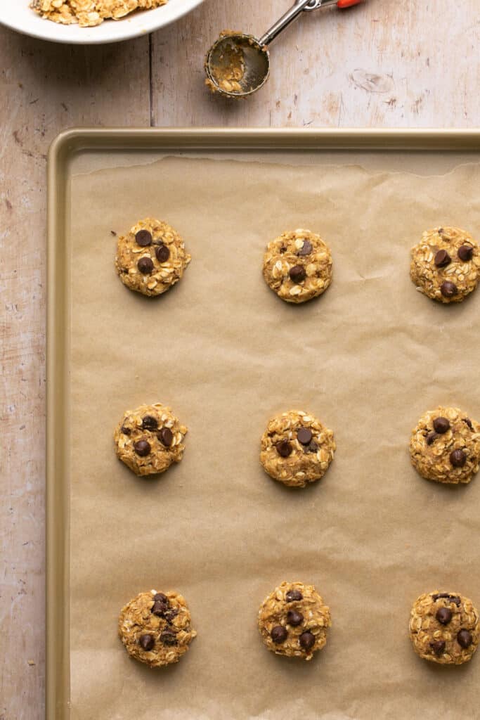 Flattened cookie dough balls on a baking sheet with parchment paper.