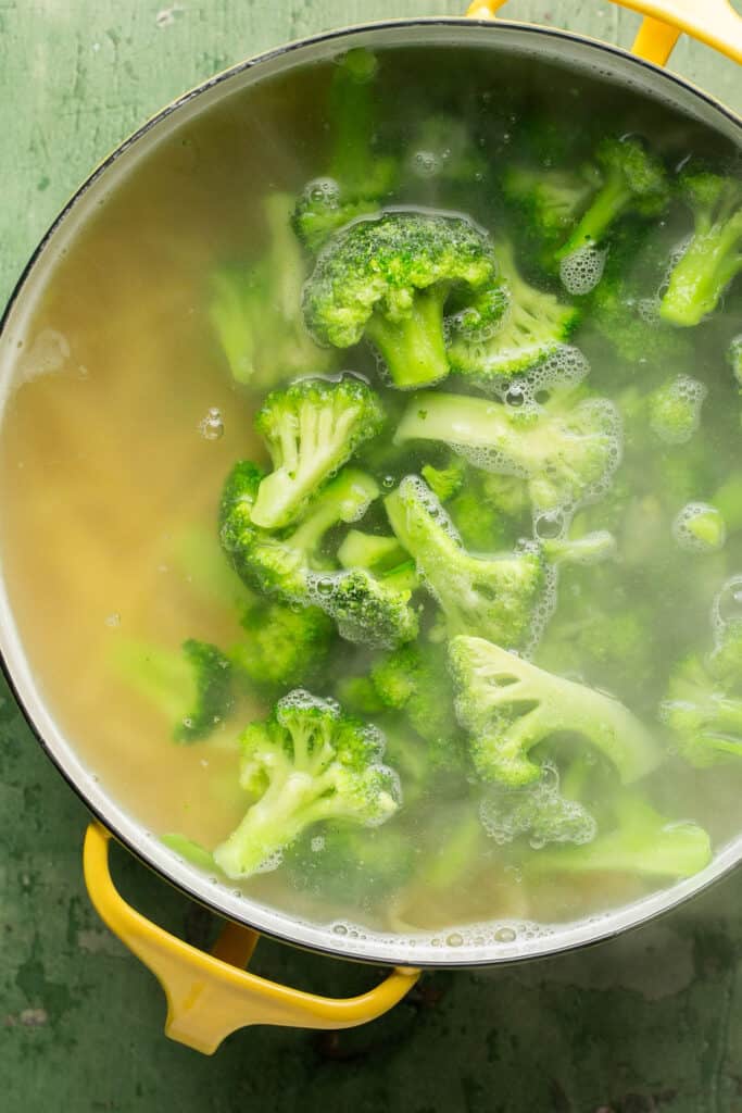 Chopped broccoli and pasta cooking in a pot of boiling water.