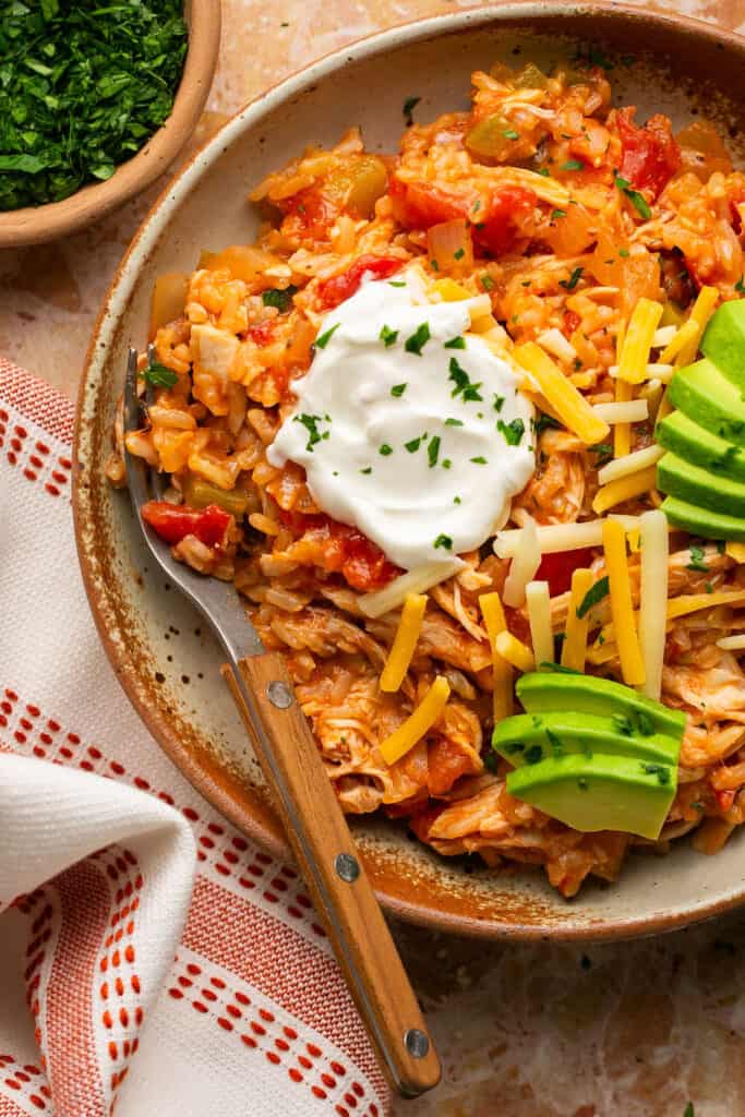 Spanish chicken and rice topped with avocado, sour cream, and shredded cheese on a plate with a fork.