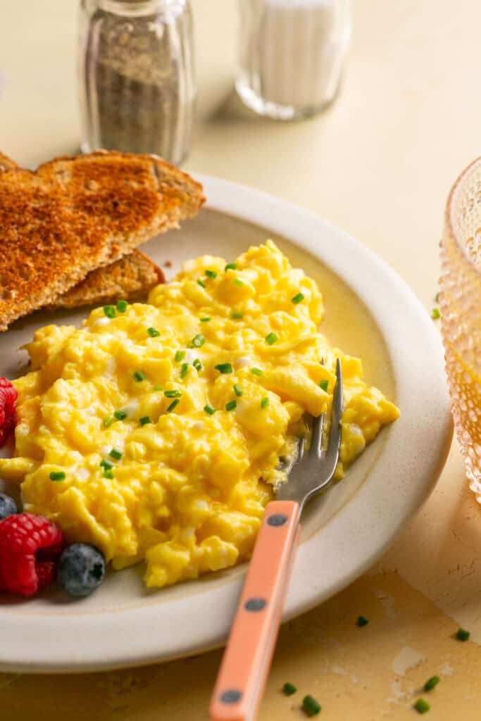 Scrambled eggs with cottage cheese with toast and berries on a plate with a fork.