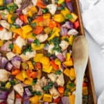 Sheet pan balsamic chicken and peppers on a baking sheet with a wooden spoon.