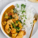 Curry chicken and cauliflower skillet on a plate with a fork with a side of rice sprinkled with cilantro.