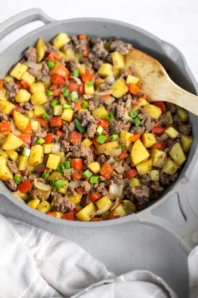 Ground beef and potato skillet in a skillet with a wooden spoon.