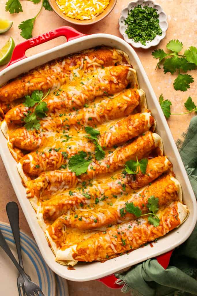 High protein chicken enchiladas topped with melty cheese and cilantro in a baking dish.