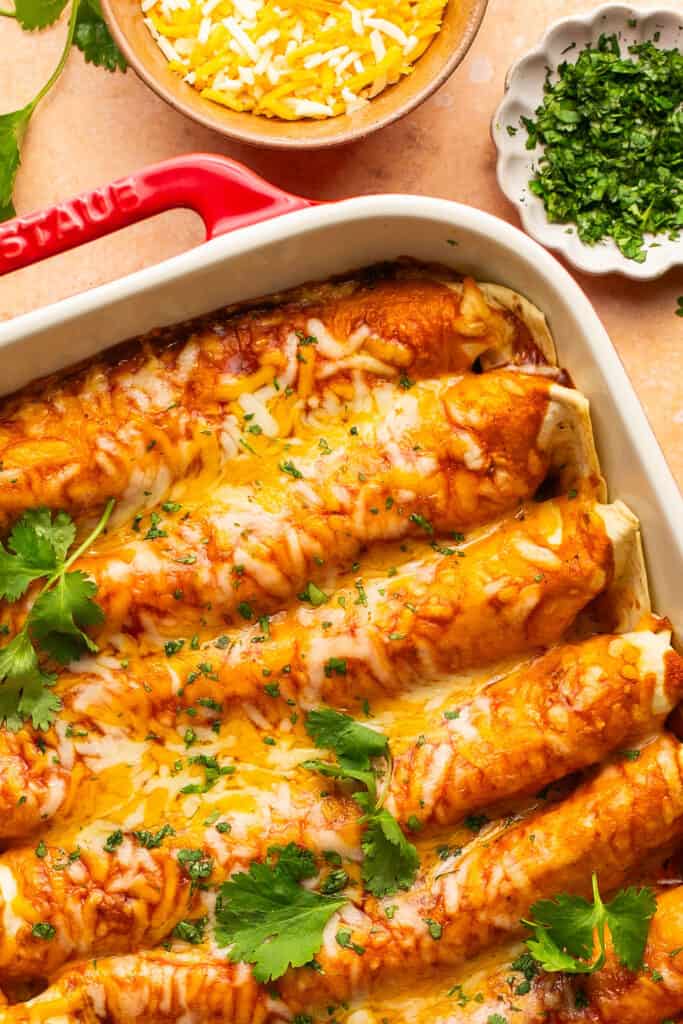 Zoomed in view of  high protein chicken enchiladas topped with melty cheese and cilantro in a baking dish.