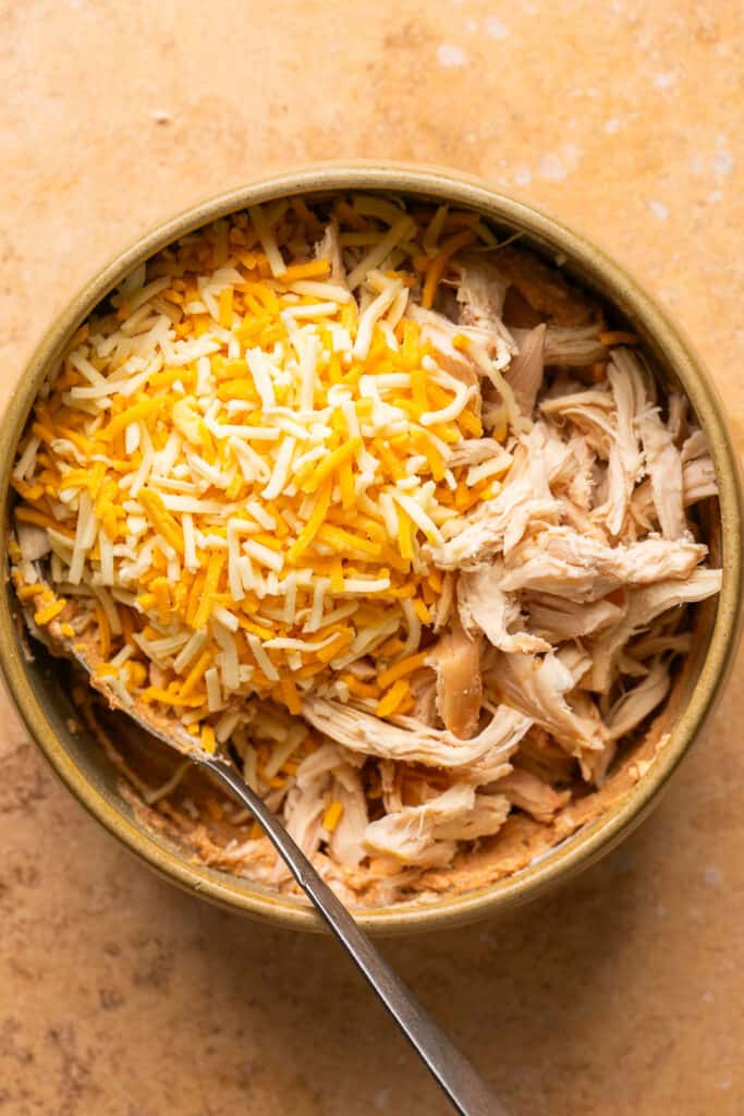 Chicken and cheese added to the mixture in a small bowl with a fork.