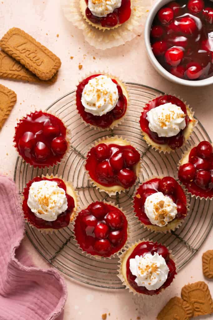No bake mini cherry cheesecakes some topped with whippped topping and some without on a cooling rack.
