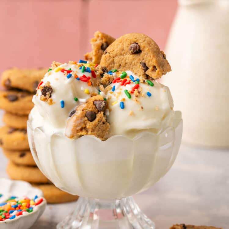 Ninja creami vanilla protein ice cream topped with chocolate chip cookie pieces and rainbow sprinkles in a glass bowl.