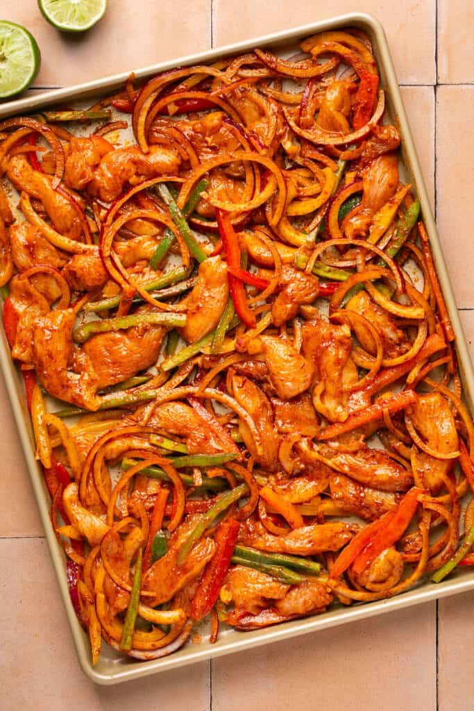 Chicken fajitas with taco seasoning on a baking sheet before being baked.
