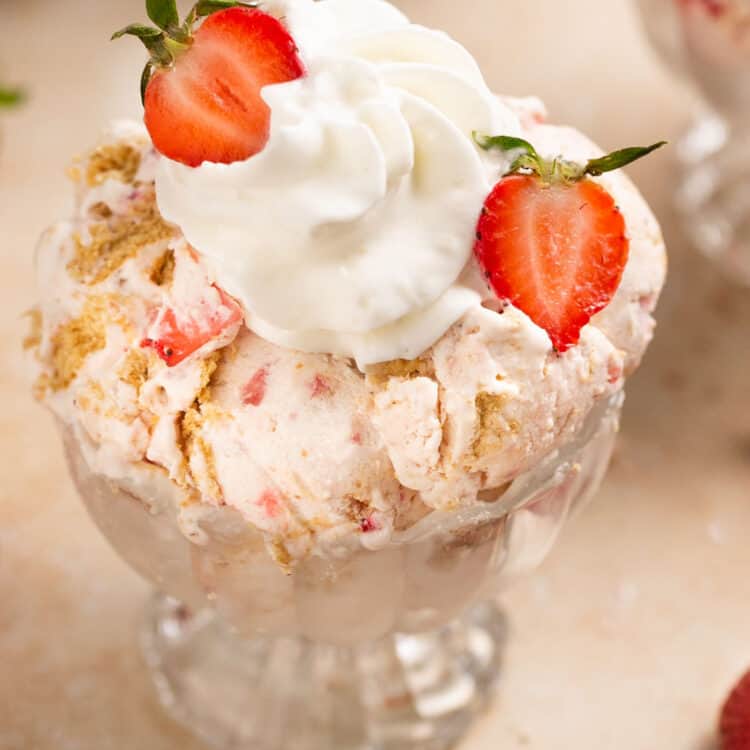 Strawberry cheesecake ninja creami protein ice cream in a glass dish topped with whipped cream and strawberries.