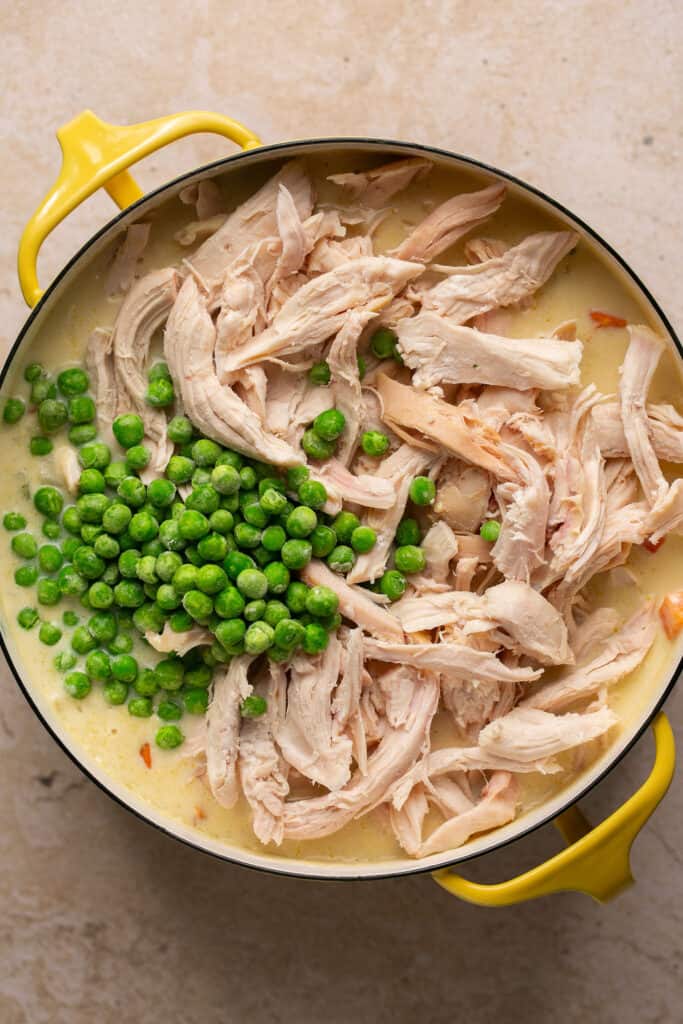 Cooked chicken and peas being added to the soup mixture in the pot.