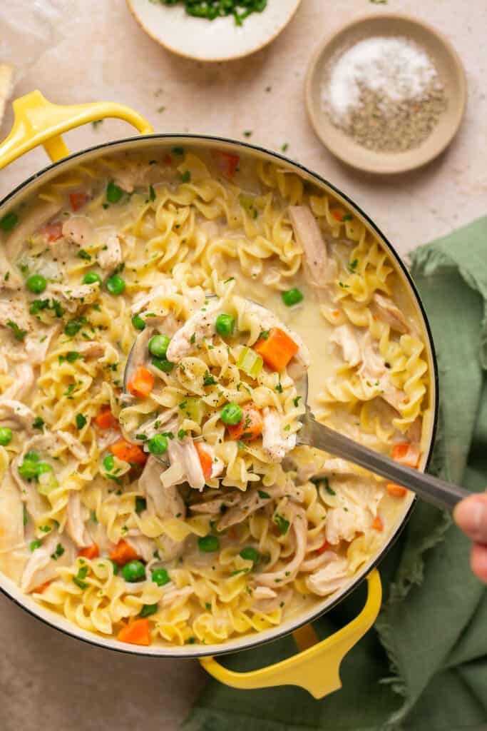 Creamy chicken noodle soup with rotisserie chicken in a pot with a spoon.