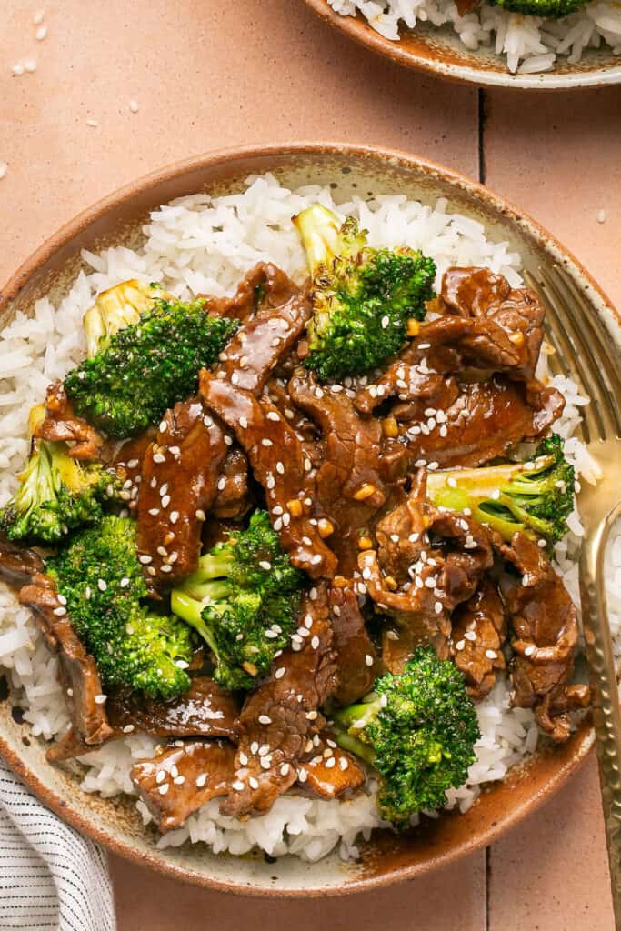 one skillet steak and broccoli served over rice on a plate with a fork.