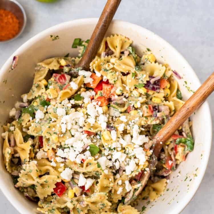 Cilantro lime pasta salad in a large bowl with a wooden spoon topped with cotija cheese.