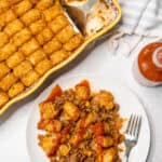 Healthier tater tot casserole in a baking dish being served on a plate with a fork.