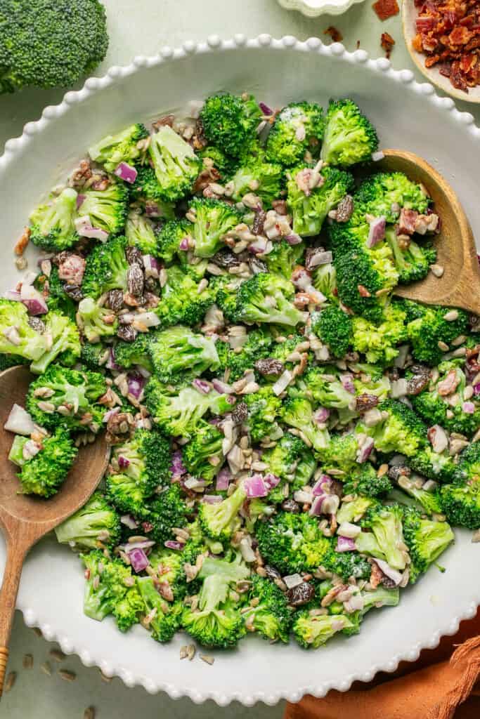 Healthy broccoli salad with greek yogurt in bowl with wooden serving spoons.