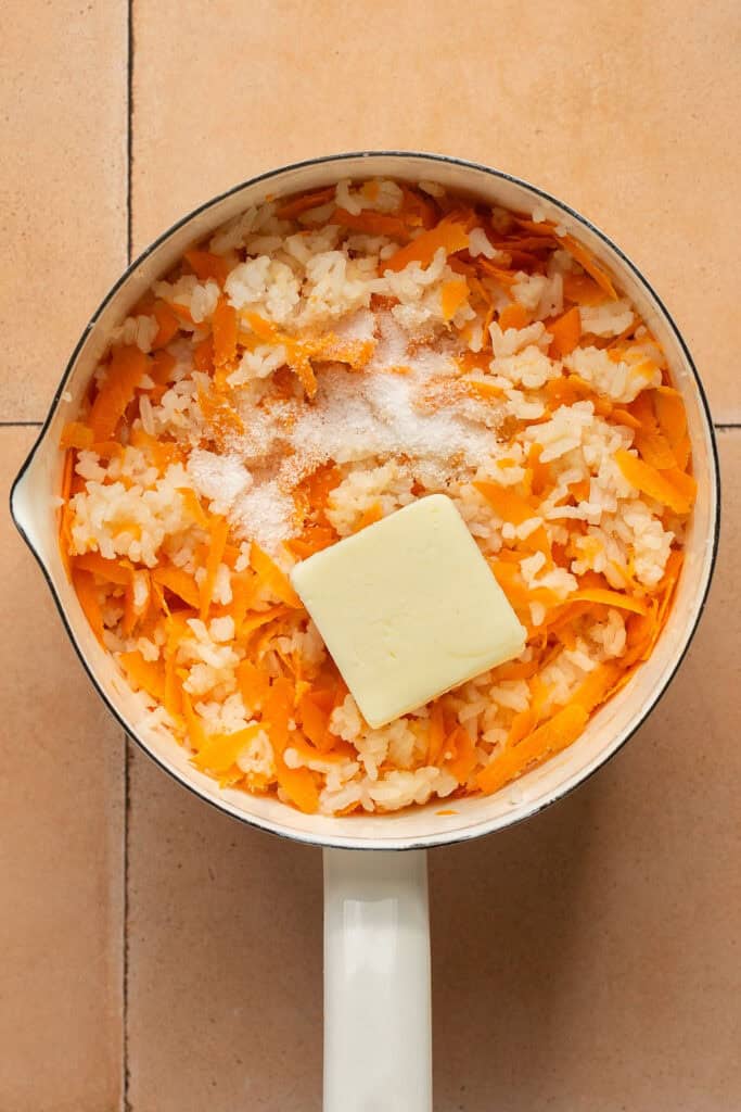 Cooked rice and shredded carrots in a saucepan topped with a square of butter.