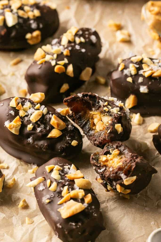 Date snickers topped with chopped peanuts and flake salt on parchment paper.