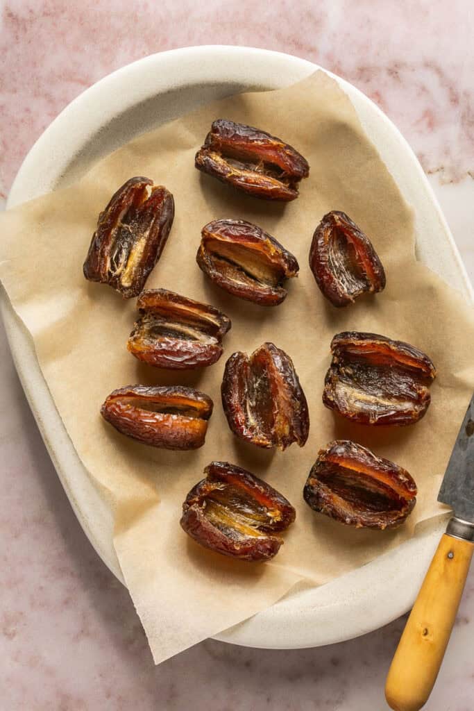 Dates cut open and pits removed on a plate with parchment paper.