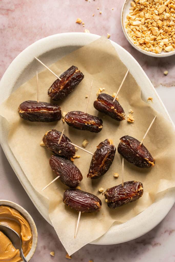 Dates stuffed with peanut butter and chopped peanuts heled together with toothpicks on a plate with parchment paper.