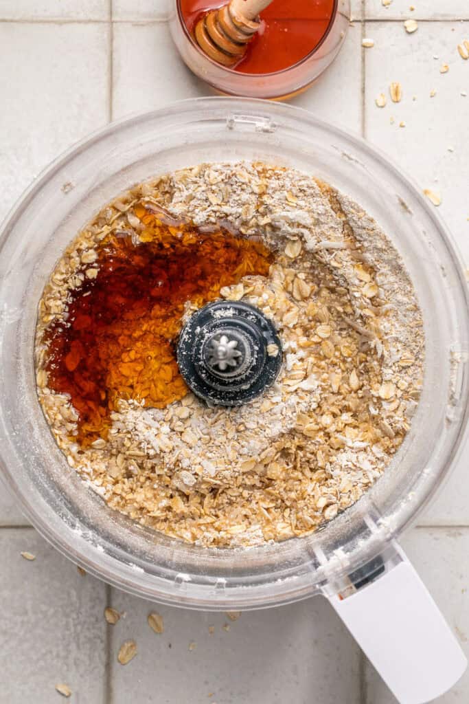 Wet ingredients added to the dry ingredients in a food processor bowl.