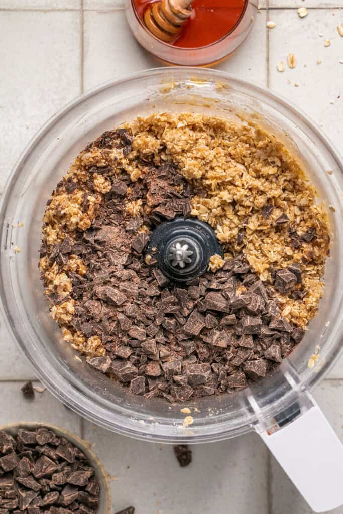 Chocolate being added to the rest of the ingredients in a food processor bowl.