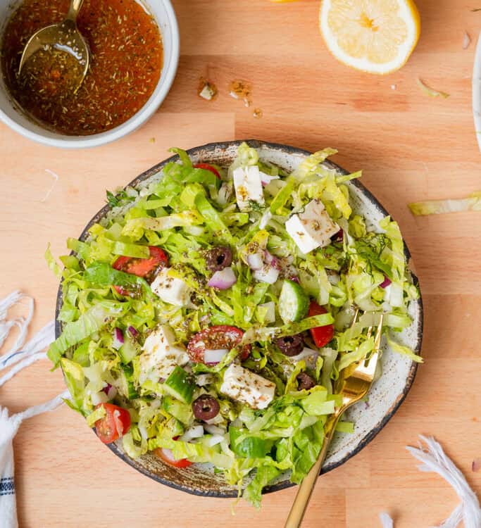 Chopped greek salad in a bowl with dressing on the side.