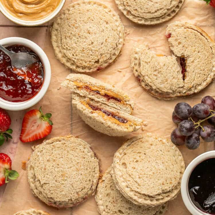 Homemade uncrustables, some cut in half, with sides of peanut butter and jelly.