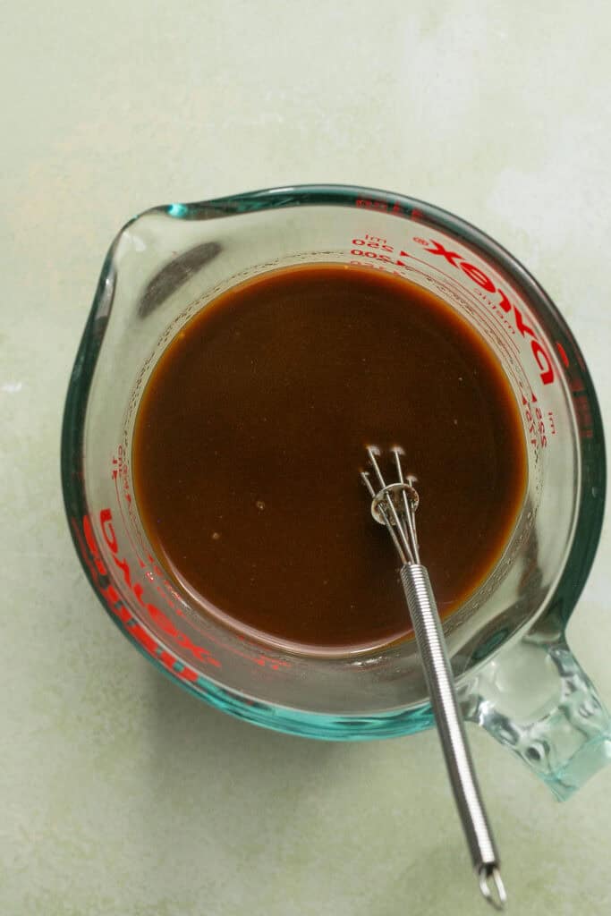 Sauce ingredients in a glass measuring cup with a whisk.