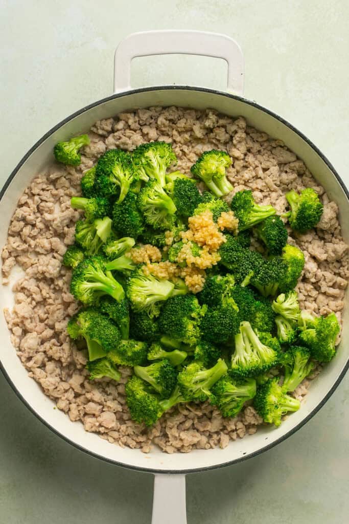 Chopped broccoli and cooked ground chicken in skillet topped with minced garlic.