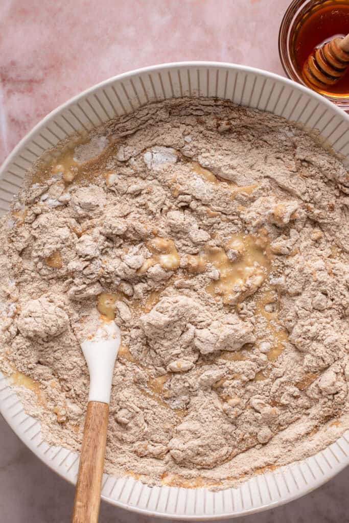 Dry ingredients mixed into the wet ingredients in a bowl with a wooden spoon.