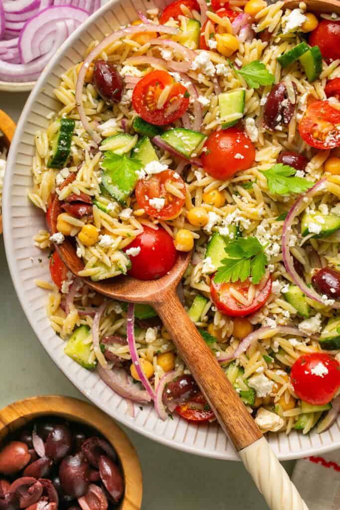 Zoomed in view of mediterranean chickpea and orzo pasta salad in a large bowl with a wooden spoon.