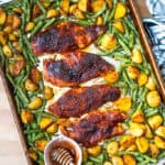 Sheet pan honey bbq chicken dinner on a baking sheet with a small bowl of honey.