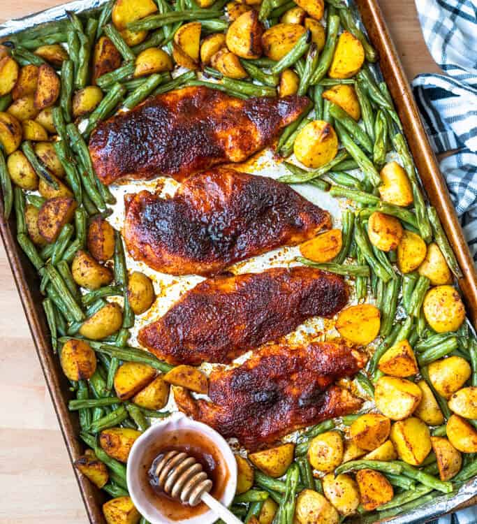 Sheet pan honey bbq chicken dinner on a baking sheet with a small bowl of honey.