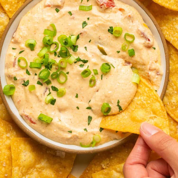 Cottage cheese queso recipe in a bowl topped with green onions with tortilla chips on the side.