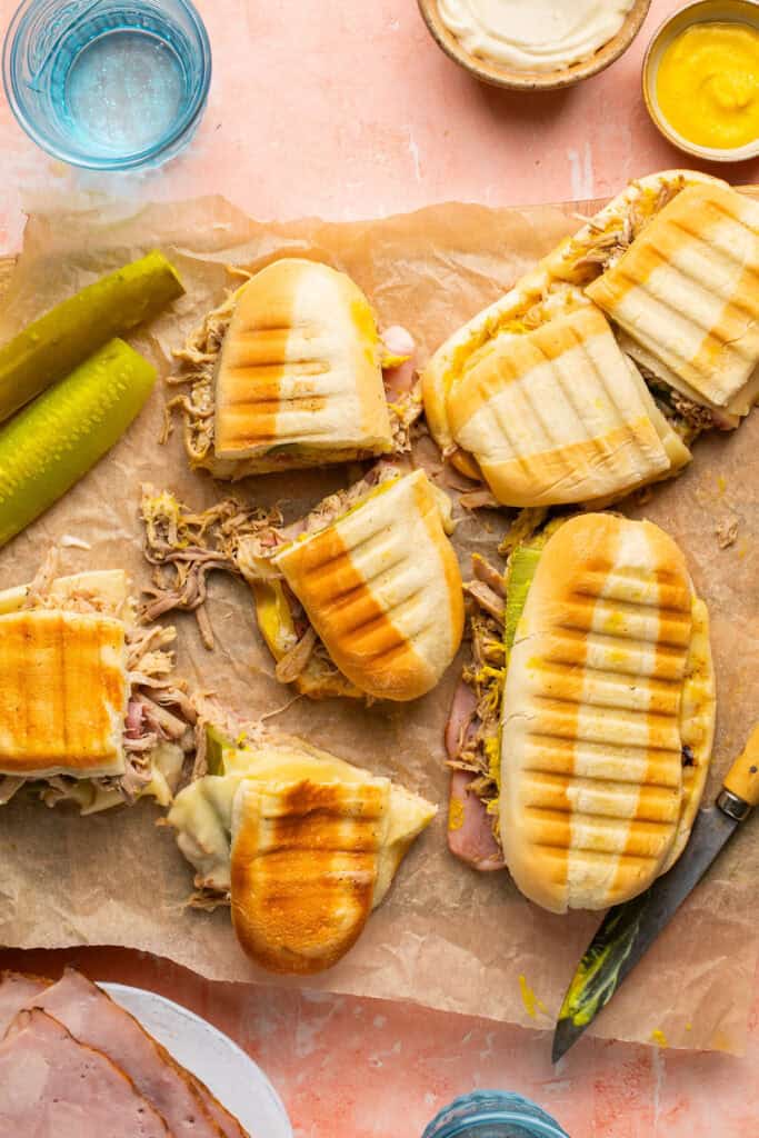 Cuban pulled pork sandwiches cut in half on parchment paper.