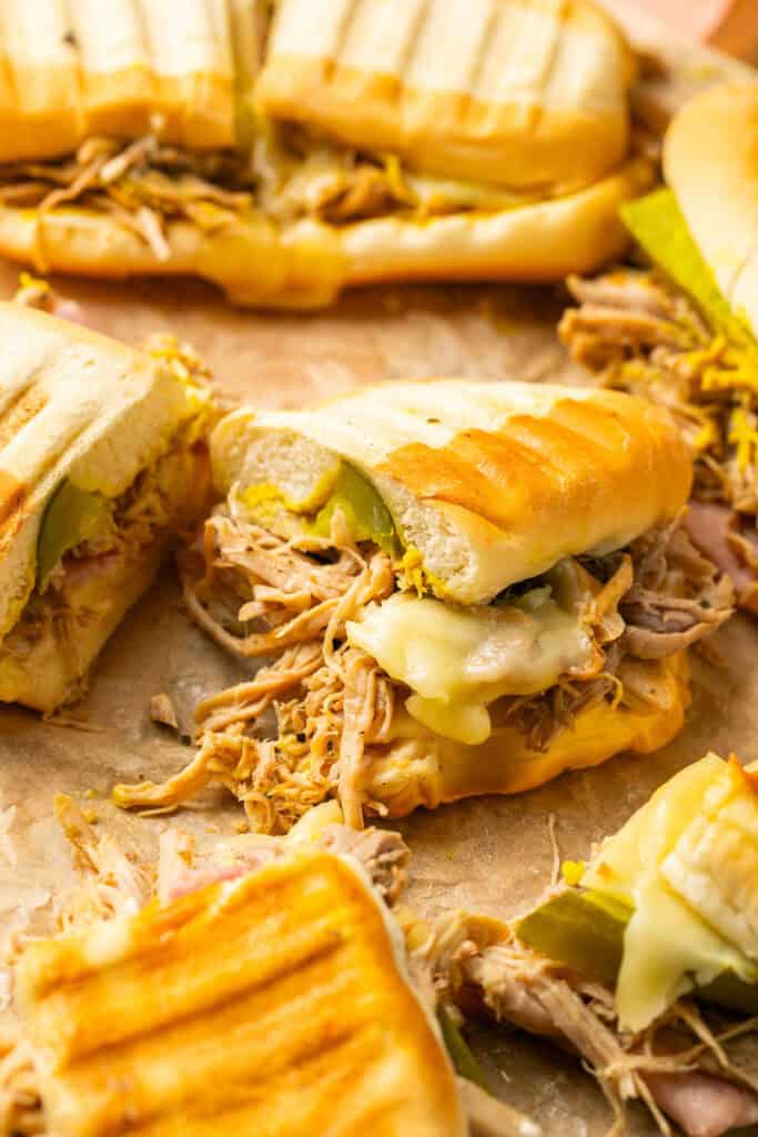 Cuban pulled pork sandwiches cut in half on parchment paper.