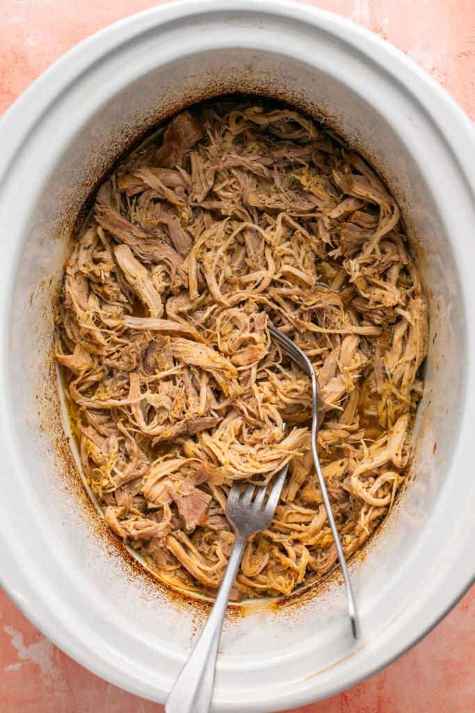 Cooked pork being shredded with 2 forks.