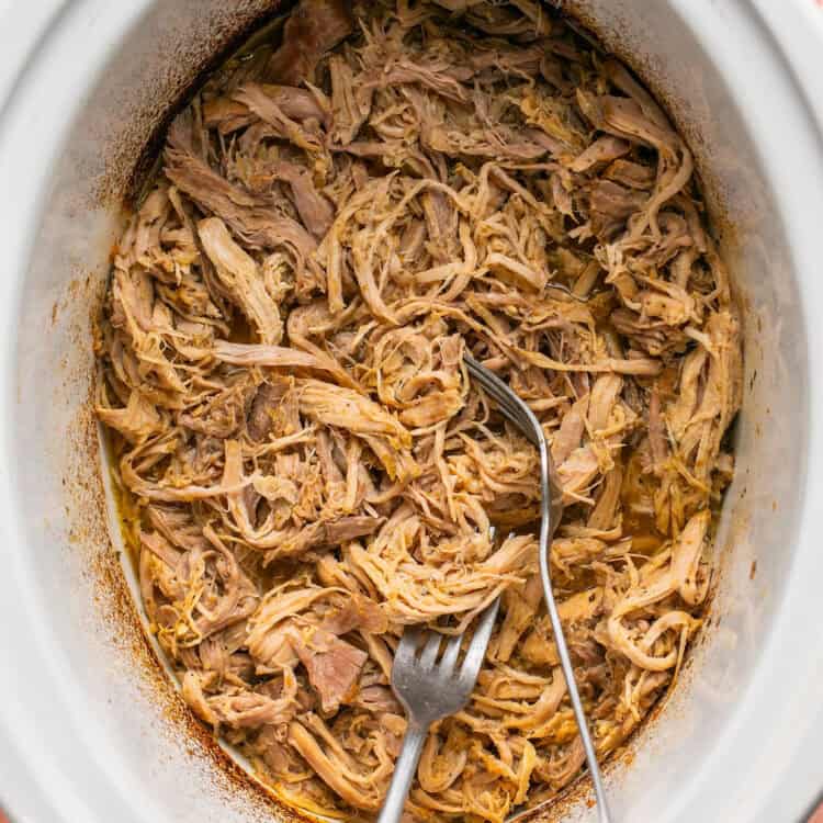 Cooked pork being shredded with 2 forks.