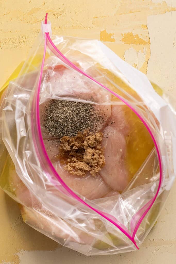 Raw chicken breasts in a zip lock bag with marinade ingredients.